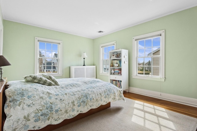 bedroom with visible vents, ornamental molding, baseboards, and wood finished floors