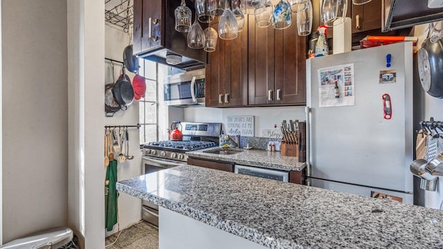 kitchen featuring dark brown cabinets, light stone countertops, appliances with stainless steel finishes, and a sink