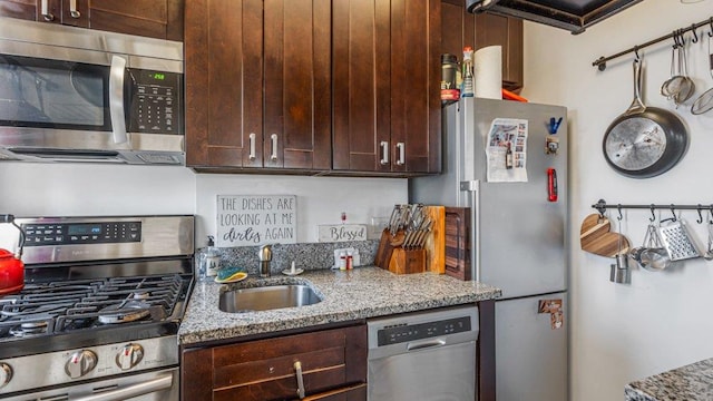 kitchen featuring dark brown cabinets, light stone countertops, appliances with stainless steel finishes, and a sink