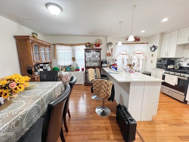 kitchen with a wealth of natural light, a kitchen breakfast bar, white cabinets, light wood finished floors, and stainless steel range with gas stovetop