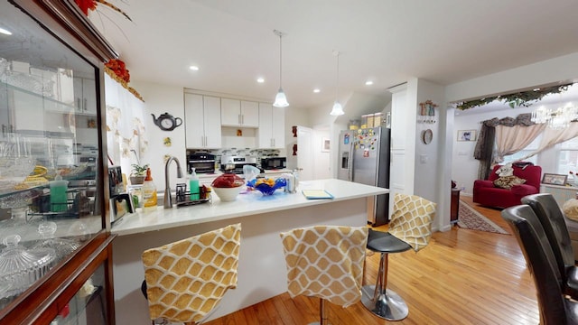 kitchen featuring light wood-type flooring, a breakfast bar, backsplash, white cabinets, and stainless steel fridge with ice dispenser