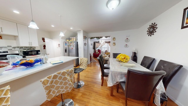 kitchen with backsplash, a breakfast bar, light wood-type flooring, white cabinets, and stainless steel appliances