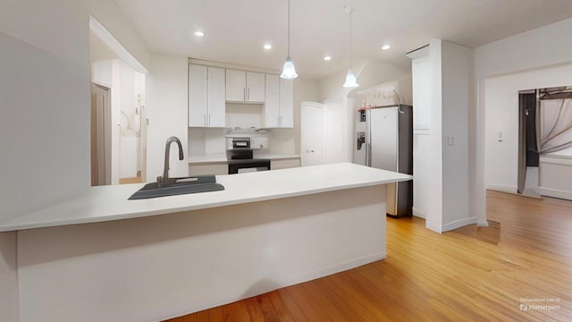 kitchen featuring a sink, a peninsula, light wood-style floors, stainless steel refrigerator with ice dispenser, and range