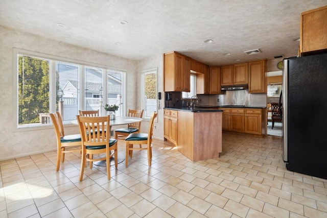 kitchen with a sink, under cabinet range hood, dark countertops, freestanding refrigerator, and light tile patterned floors