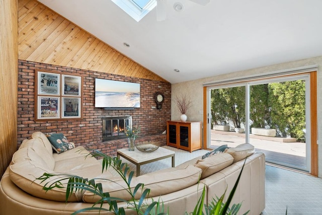 living area with vaulted ceiling with skylight, a brick fireplace, brick wall, and ceiling fan