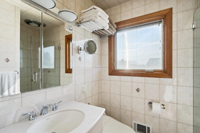 full bathroom featuring visible vents, toilet, a sink, tile walls, and a shower stall