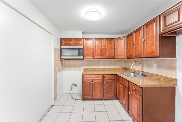 kitchen featuring a sink, stainless steel microwave, light countertops, light tile patterned floors, and decorative backsplash