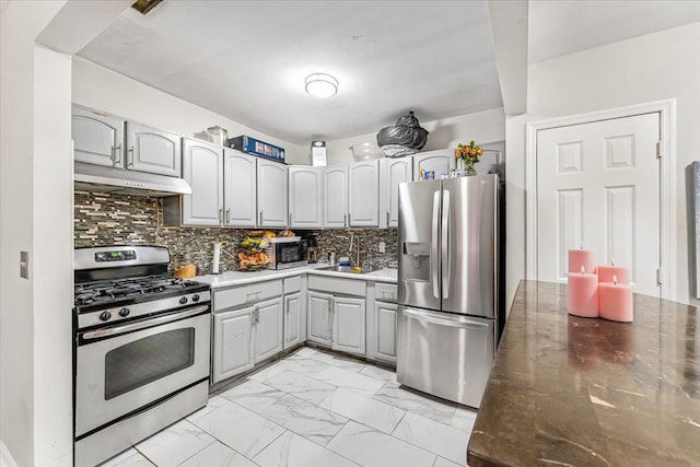 kitchen featuring a sink, stainless steel appliances, marble finish floor, under cabinet range hood, and tasteful backsplash