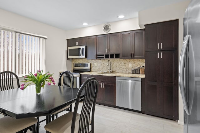 kitchen with light stone countertops, a sink, dark brown cabinets, appliances with stainless steel finishes, and tasteful backsplash