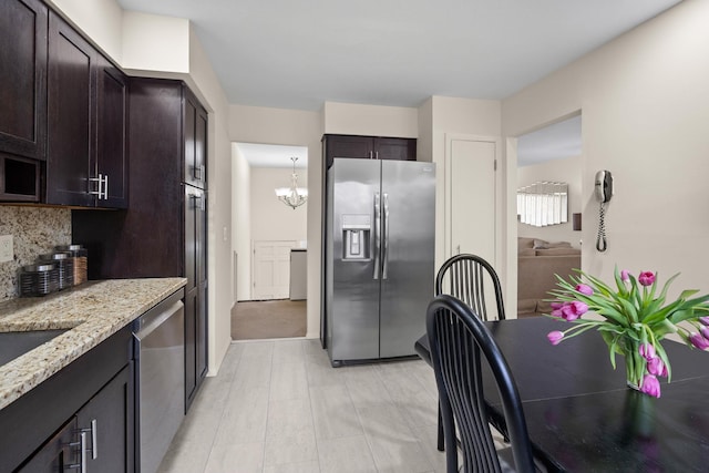 kitchen with backsplash, light stone countertops, dark brown cabinetry, appliances with stainless steel finishes, and an inviting chandelier