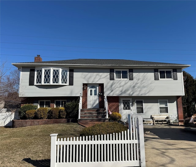 split foyer home featuring a fenced front yard, brick siding, a chimney, and entry steps