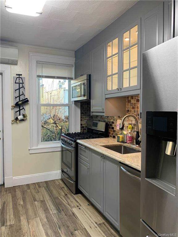 kitchen with an AC wall unit, gray cabinets, appliances with stainless steel finishes, light wood-style floors, and a sink