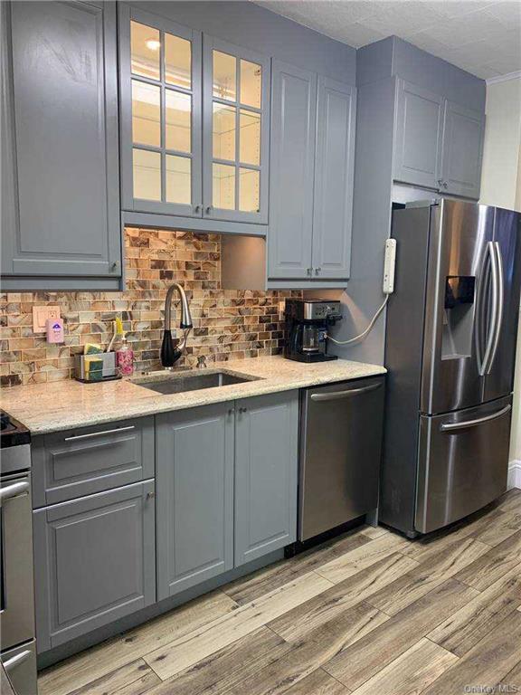 kitchen featuring tasteful backsplash, gray cabinets, appliances with stainless steel finishes, light wood-style floors, and a sink