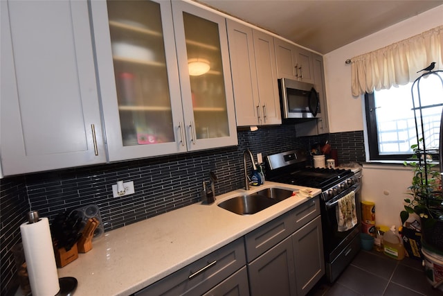 kitchen featuring dark tile patterned floors, a sink, stainless steel microwave, tasteful backsplash, and black range with gas cooktop