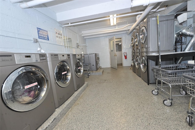 shared laundry area featuring washer and clothes dryer, concrete block wall, and stacked washing maching and dryer