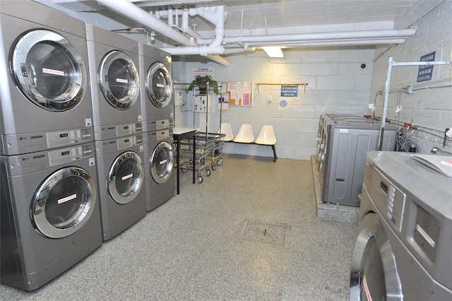 community laundry room featuring washing machine and clothes dryer, concrete block wall, and stacked washing maching and dryer