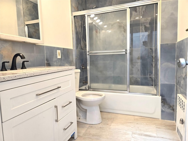 bathroom featuring toilet, combined bath / shower with glass door, radiator, tile walls, and vanity