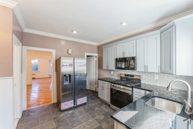 kitchen with dark stone countertops, a sink, ornamental molding, stainless steel appliances, and backsplash