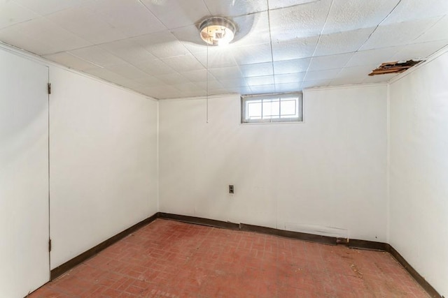 below grade area with a drop ceiling, brick floor, and baseboards