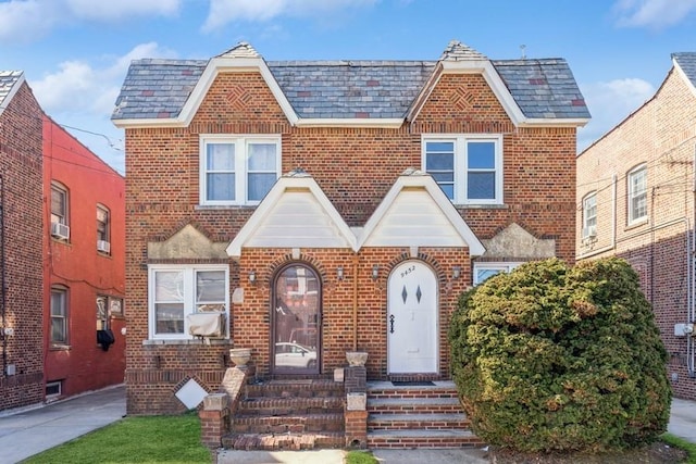 tudor house featuring a high end roof, cooling unit, and brick siding