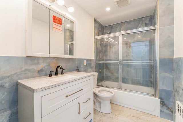 bathroom featuring vanity, visible vents, enclosed tub / shower combo, tile walls, and toilet