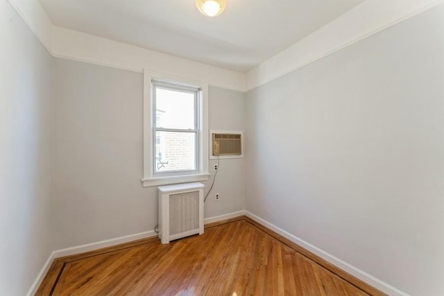 unfurnished room with an AC wall unit, radiator, baseboards, and light wood-type flooring