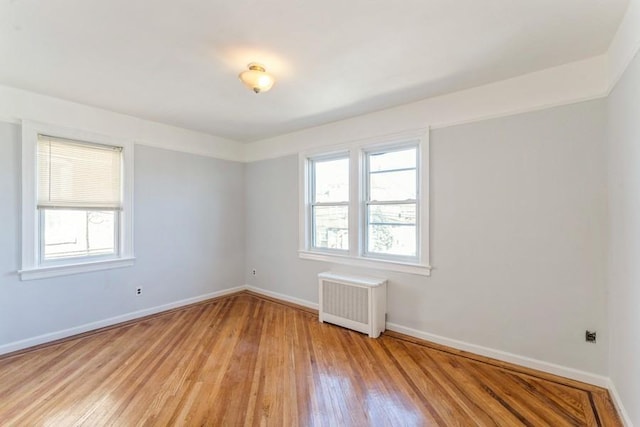 unfurnished room with light wood finished floors, radiator heating unit, baseboards, and a wealth of natural light