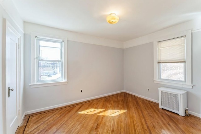 unfurnished room featuring radiator heating unit, wood finished floors, and baseboards