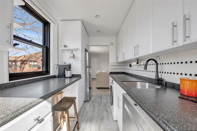 kitchen featuring backsplash, washer / dryer, appliances with stainless steel finishes, white cabinetry, and a sink