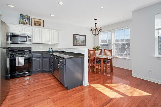 kitchen with dark countertops, black gas stove, light wood-style floors, white cabinetry, and stainless steel microwave