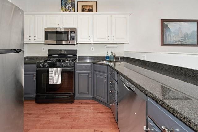 kitchen featuring gray cabinetry, light wood-style flooring, white cabinets, stainless steel appliances, and a sink