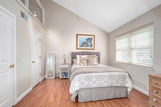 bedroom with visible vents, light wood-type flooring, baseboards, and vaulted ceiling