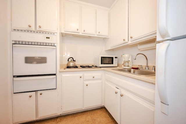 kitchen with tasteful backsplash, light countertops, white appliances, a warming drawer, and a sink