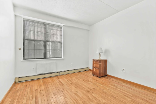 unfurnished room with a textured ceiling, a baseboard heating unit, baseboards, and hardwood / wood-style flooring