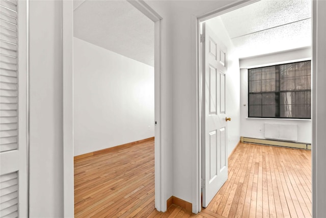 hall with a baseboard heating unit, baseboards, and wood-type flooring