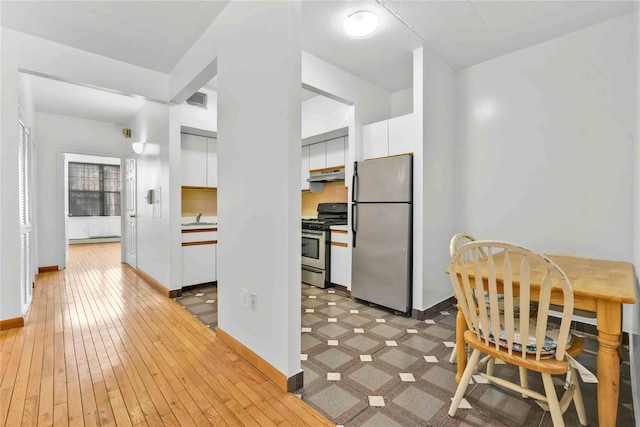 kitchen featuring visible vents, under cabinet range hood, light wood-type flooring, appliances with stainless steel finishes, and white cabinetry