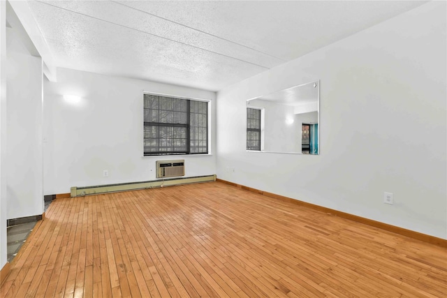 unfurnished room featuring a wall mounted air conditioner, a textured ceiling, wood-type flooring, a baseboard radiator, and baseboards