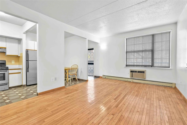 unfurnished living room with baseboards, light wood-style floors, a wall mounted air conditioner, a textured ceiling, and baseboard heating