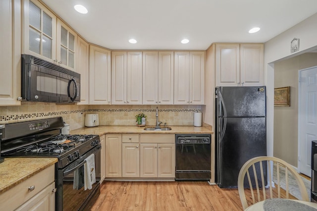 kitchen featuring tasteful backsplash, glass insert cabinets, light wood-style flooring, black appliances, and a sink