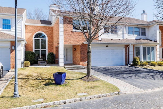 view of front of property with an attached garage, brick siding, a chimney, and driveway