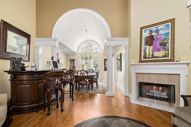 interior space with a chandelier, a fireplace with flush hearth, lofted ceiling, hardwood / wood-style floors, and ornate columns