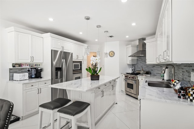 kitchen featuring a sink, appliances with stainless steel finishes, white cabinetry, wall chimney range hood, and a center island