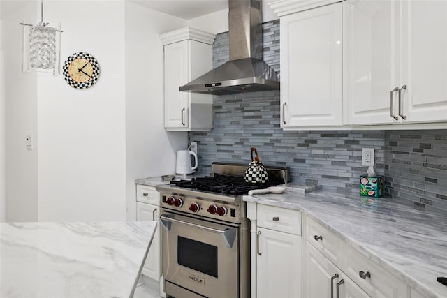 kitchen featuring designer range, backsplash, white cabinets, and wall chimney range hood