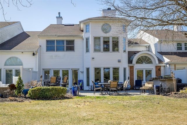 back of property featuring a patio, fence, a yard, a shingled roof, and a chimney