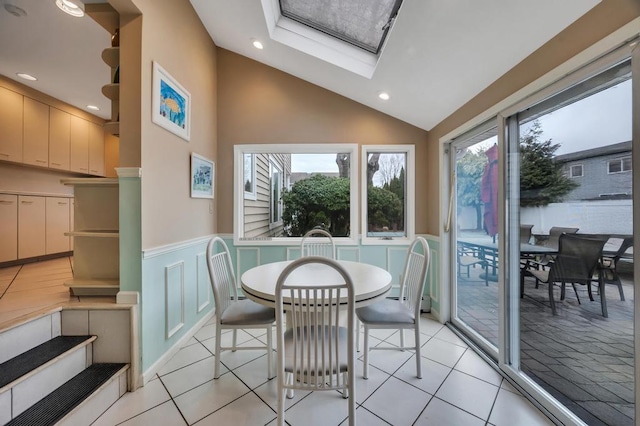 dining area featuring a wealth of natural light, a decorative wall, wainscoting, and vaulted ceiling with skylight