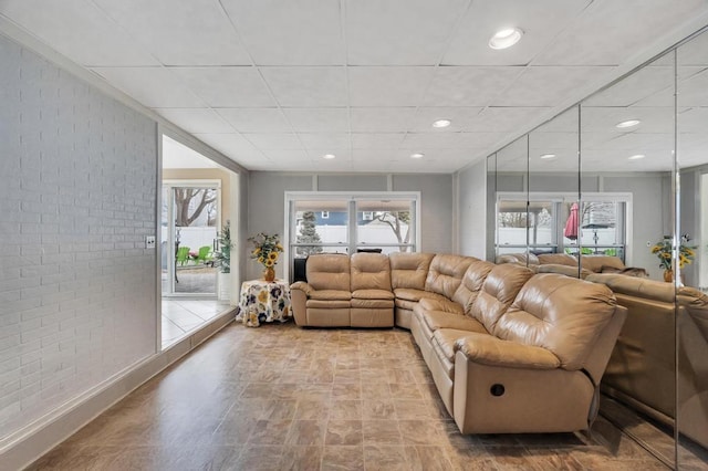 living area with recessed lighting, a drop ceiling, and brick wall