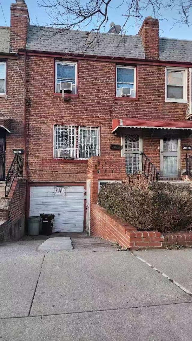 view of front facade with an attached garage, brick siding, driveway, and a chimney