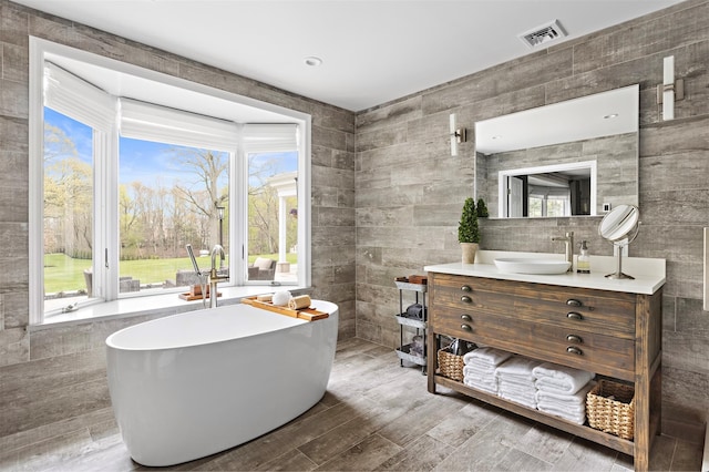 full bath with a soaking tub, visible vents, plenty of natural light, and tile walls