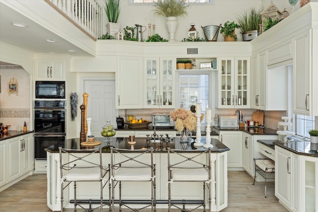 kitchen with black appliances, tasteful backsplash, dark countertops, a breakfast bar area, and light wood finished floors