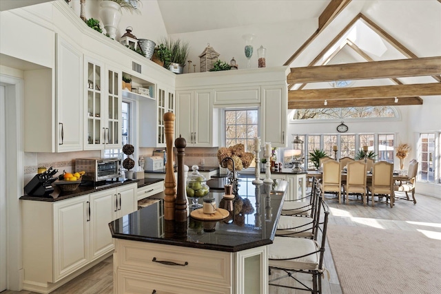 kitchen with high vaulted ceiling, light wood-style flooring, a toaster, glass insert cabinets, and a kitchen bar